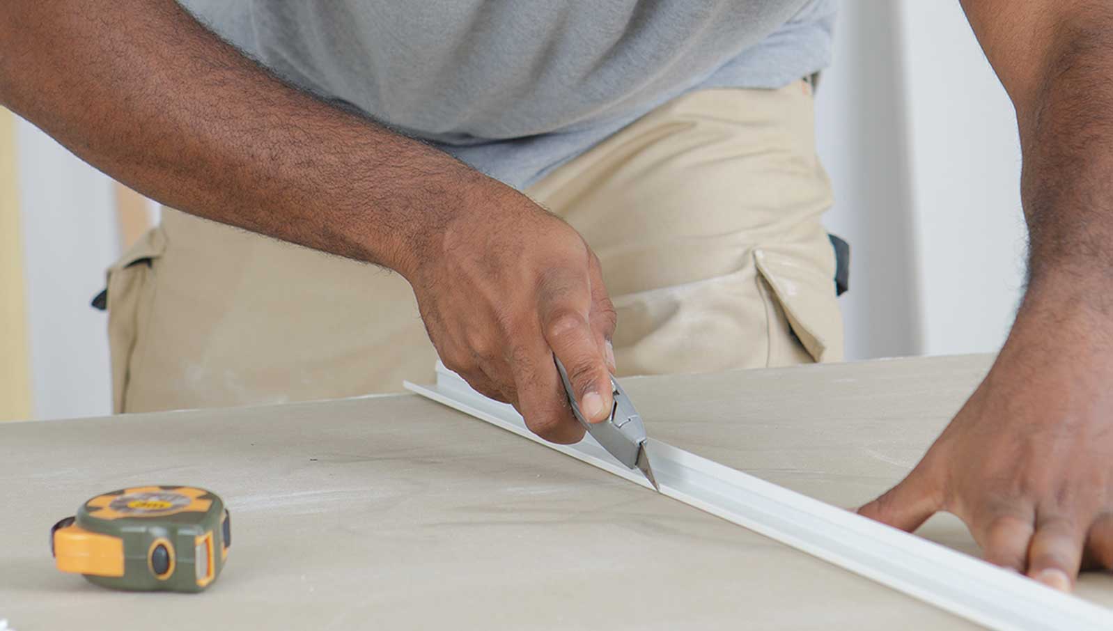 Präzises Zuschneiden eines Materials mit einem Cuttermesser Eine Person schneidet ein Material mit einem Cuttermesser, neben einem Maßband auf einem Tisch