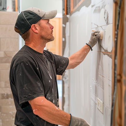 Fliesenleger bei der Arbeit: Wandverkleidung anbringen Ein Handwerker befestigt Fliesen an einer Wand in einem Innenraum